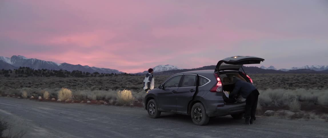 People standing around stopped car at sunset with calm reflective mood.