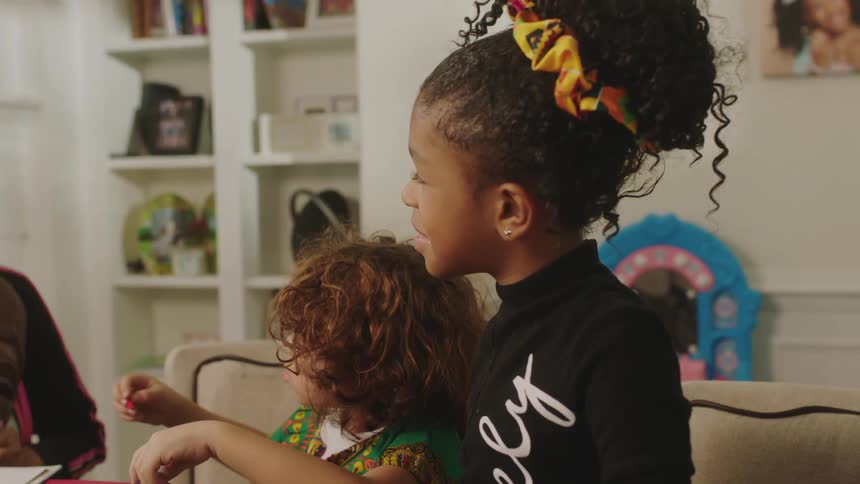 A grandmother puts on a wooden mask while telling a story to her granddaughters