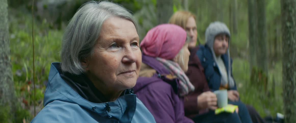 Four women sit and chat in the woods while bundled up