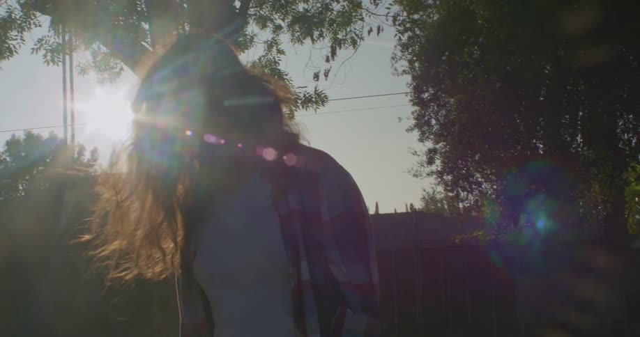 A woman standing outside in the bright sunshine tosses her long hair back and forward