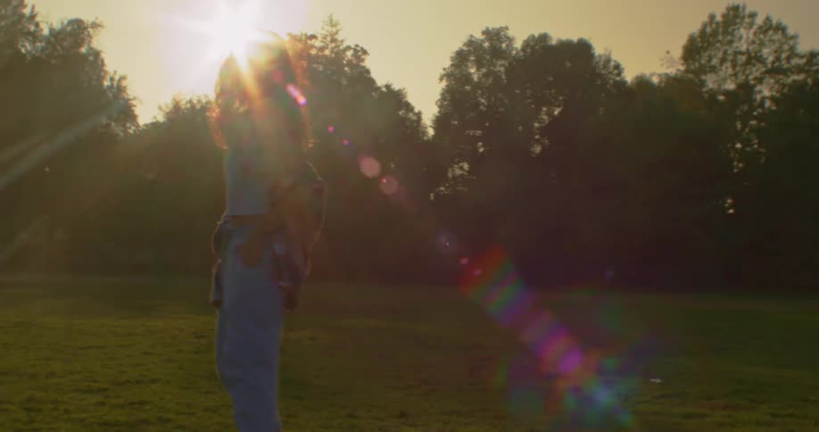 Young woman on a park at sunset walking backwards looking at the camera