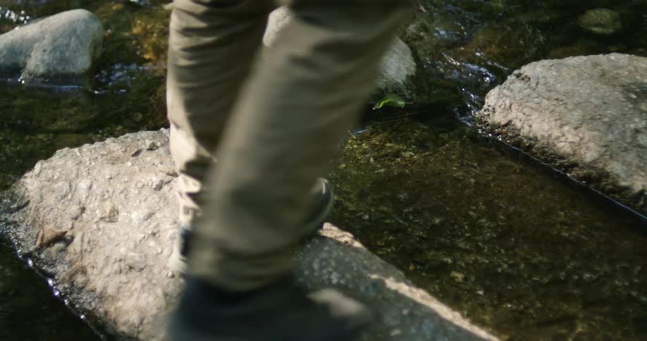 A man steps on rocks as he walks across a river