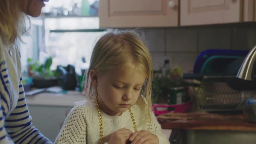 Mother teaching daughter how to peel potatoes on the kitchen sink at home