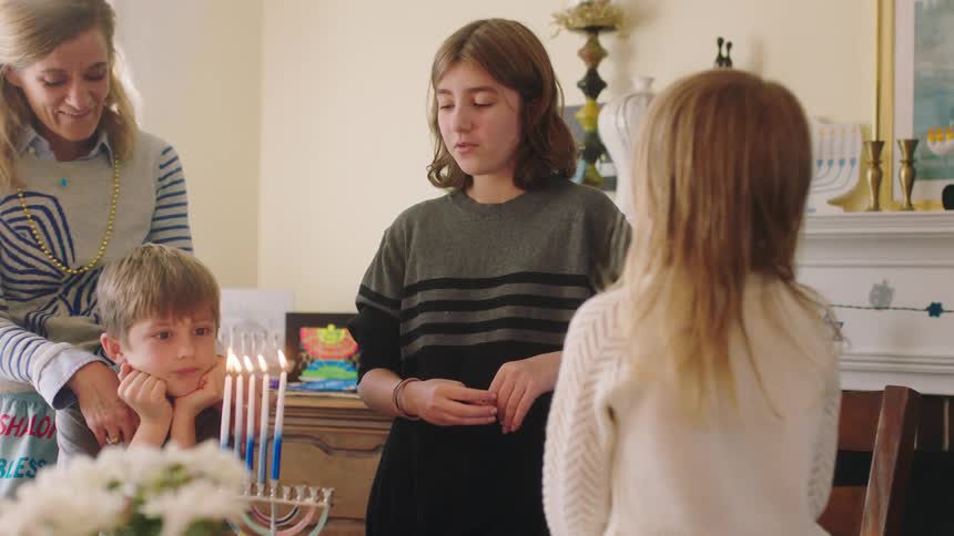 Three children and a woman gather around a table with a hanukkah candle