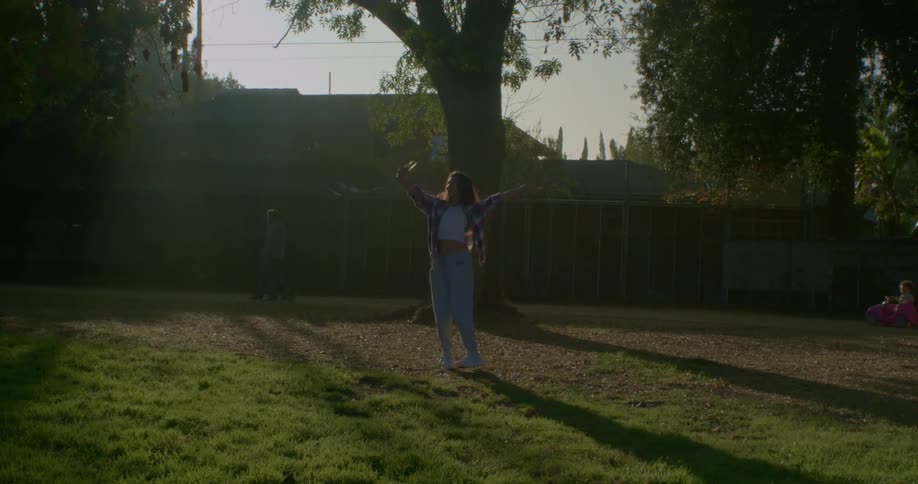 A teenager spins in a circle and takes a selfie with her cell phone as people walk past her in the background