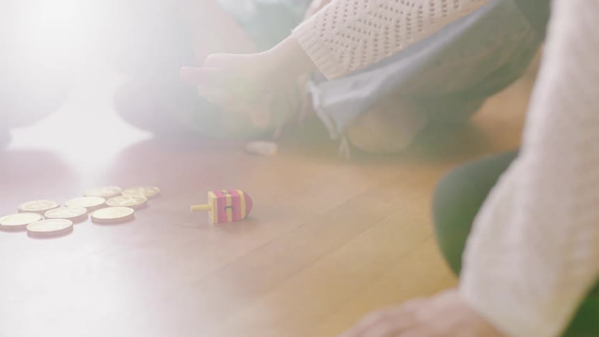 A young girl spins a dreidel toy while sitting on the floor
