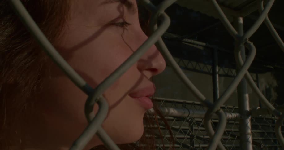 A teenage girl standing behind a chain link fence
