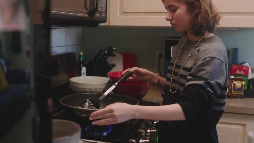 Young teenager cooking on a pan over the kitchen at home