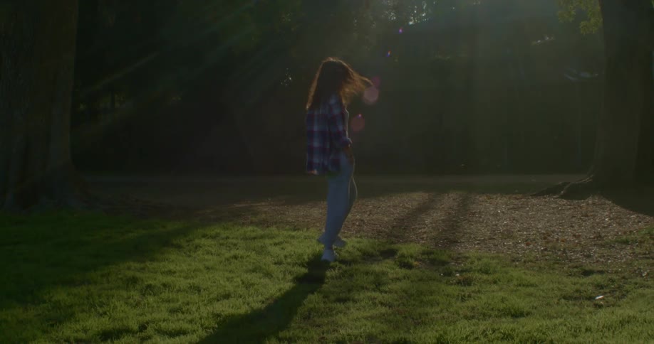 Young woman walking over the green grass on the backyard turns around to look at the camera at sunset
