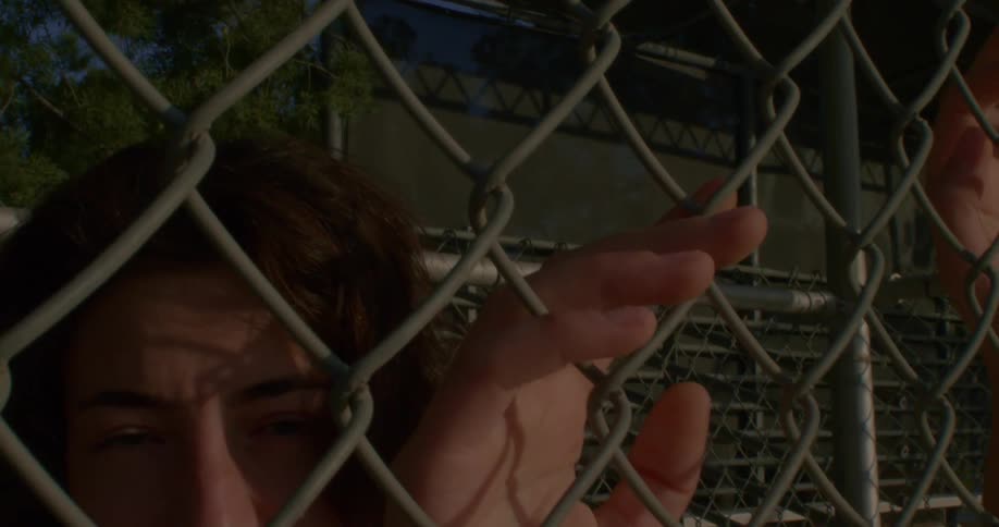A teen holds onto a chain link fence while posing under bleachers