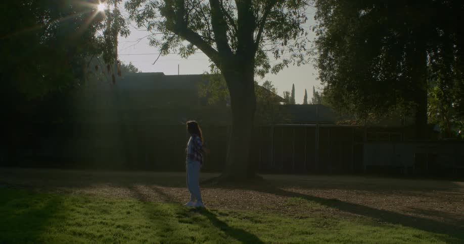 A woman stands in a back yard and looks forwards