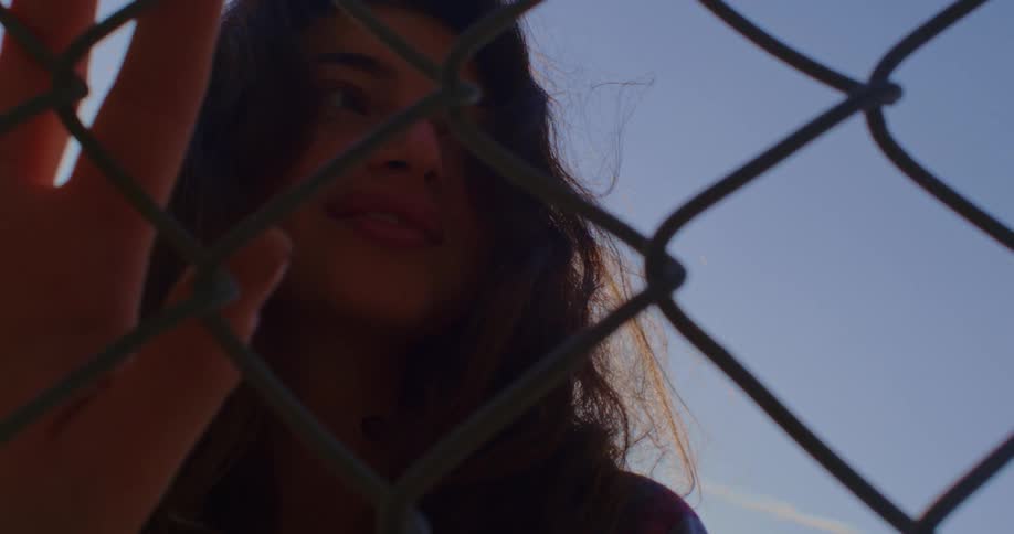 A woman is standing by a fence outdoors during the day