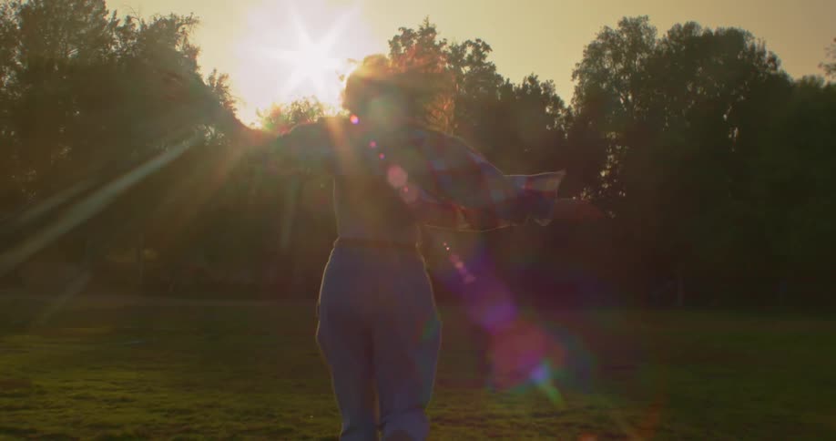 Young woman with arms wide open running towards the sunset in a park