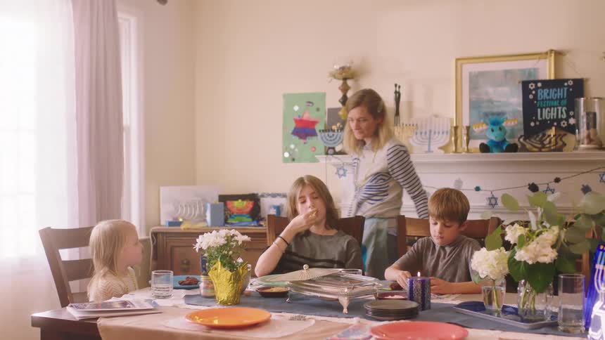 Mother walks around table as her children sit and eat