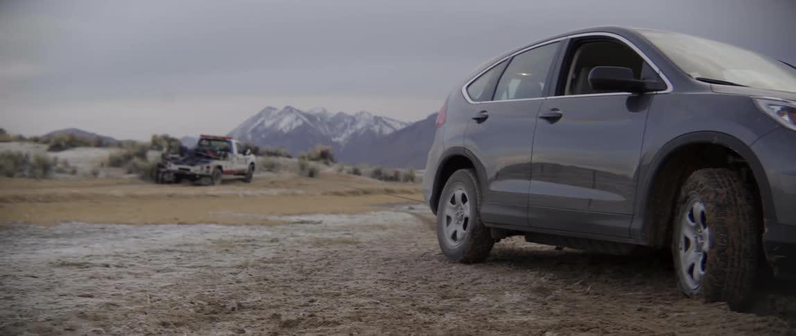 Recovery tow truck parked near a stranded SUV in a snowy mountain landscape view.