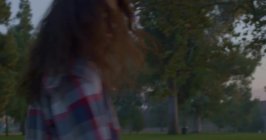 Young woman walking on the park turns around to look at the camera at sunset