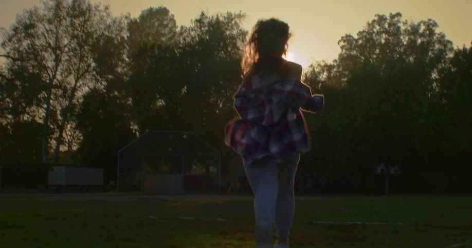 Woman runs across sports field toward sun then turns and is back lit
