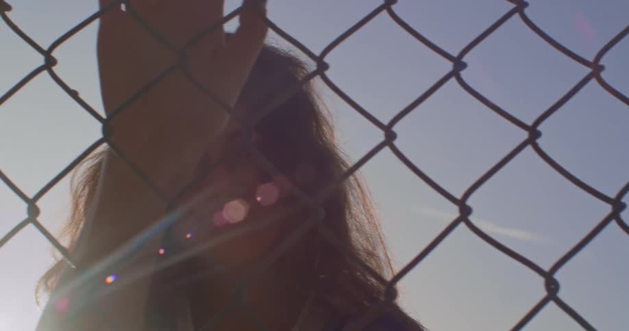 A young woman stands with her hand holding onto a chain link fence