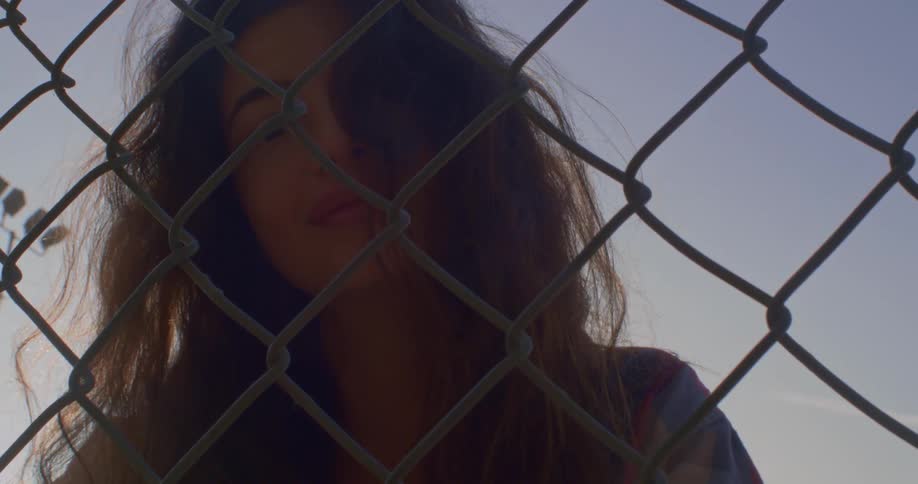 Woman looks through chain link fence with field lights in the sky behind her
