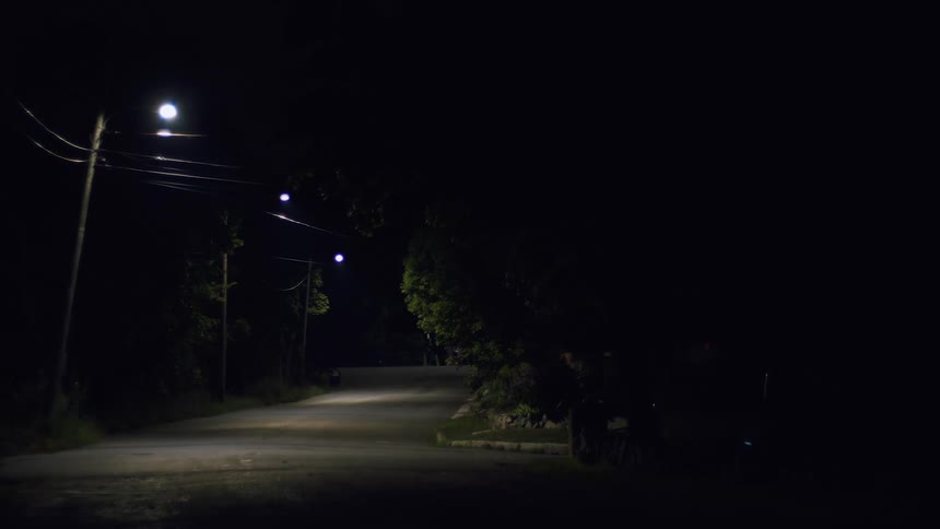 Person rides skateboard along highway passing intersection at night