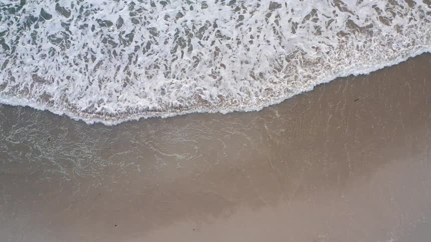 Aerial view of waves rolling over a beach splashing and foaming