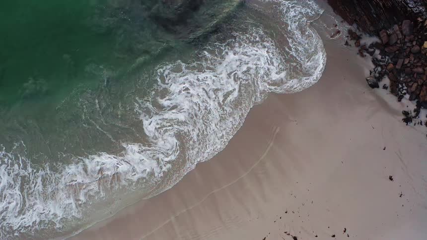 Ocean waves are rolling up onto a sandy beach near rock layers