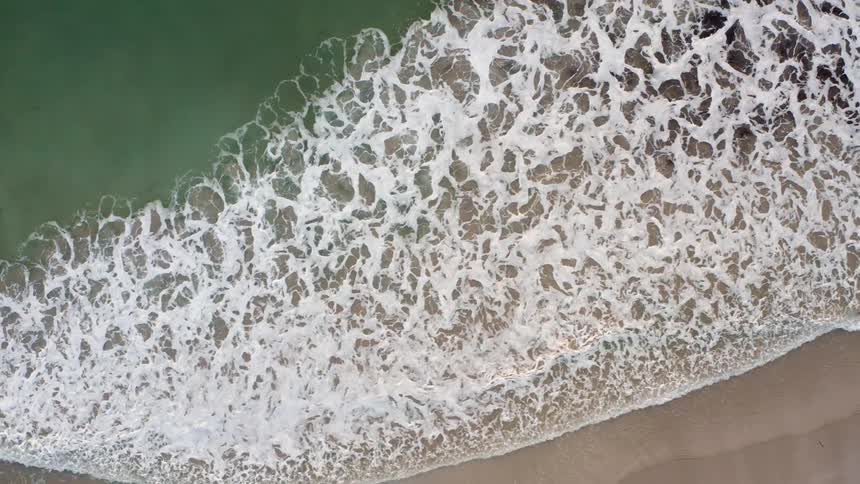 Top down aerial view of ocean waves gently washing over the beach sand