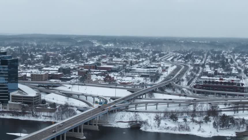 Snow covers ground as traffic flows over bridge and along highway through city