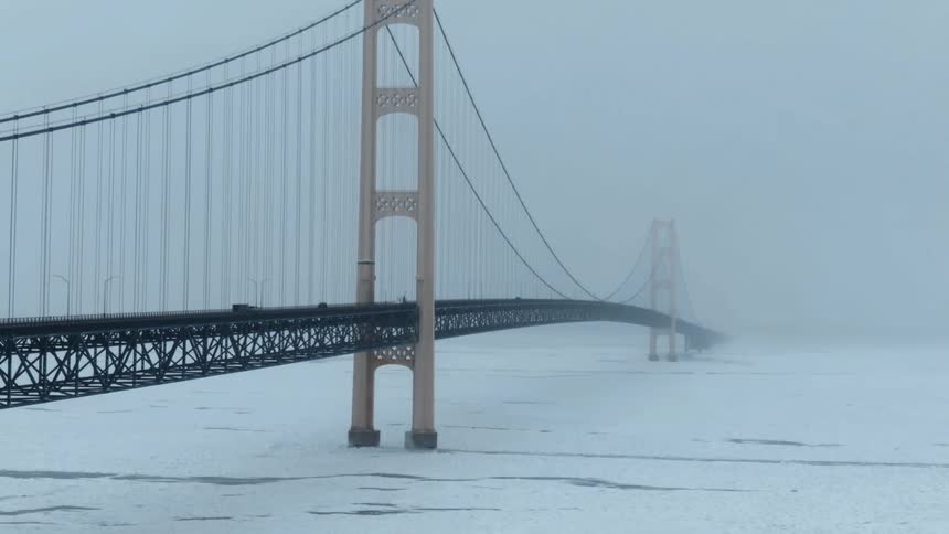 Aerial view of a suspension bridge in the fog over the frozen surface of a lake