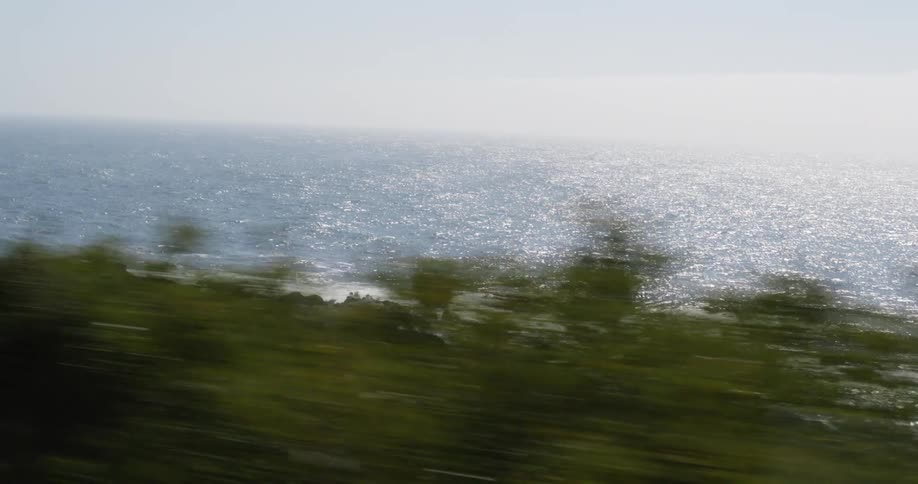 Sunlight reflecting on the surface of the ocean close to the coast seen from a moving vehicle
