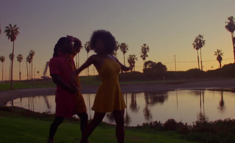 Man and woman dance on shore near pond at park against a red tinted horizon