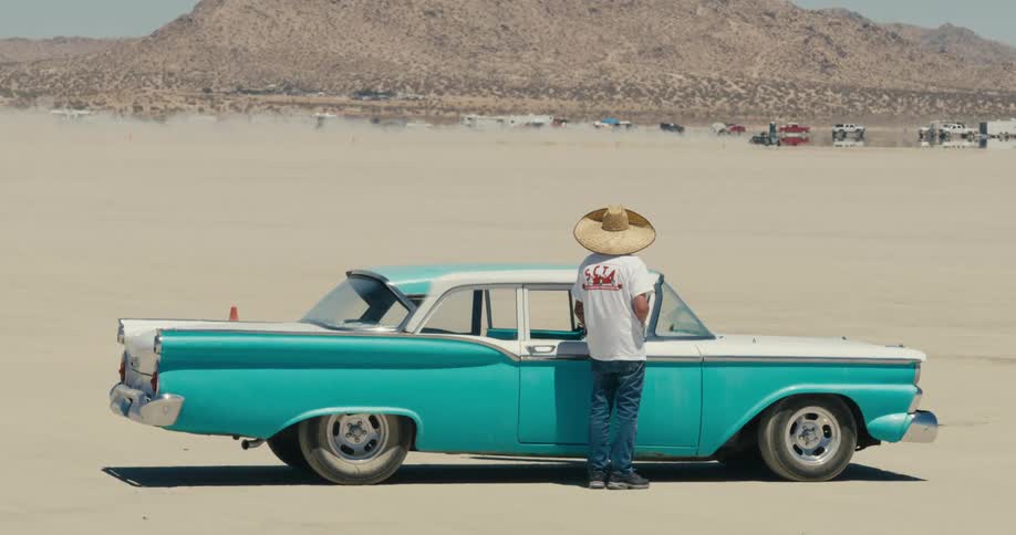 A man is standing outside of his car in the desert