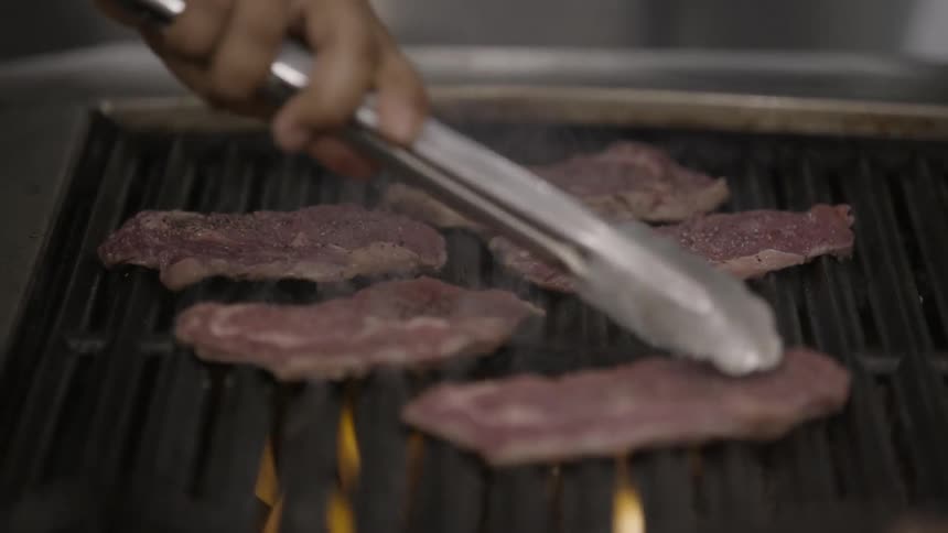 Thin cuts of meat are cooking on a bbq grill