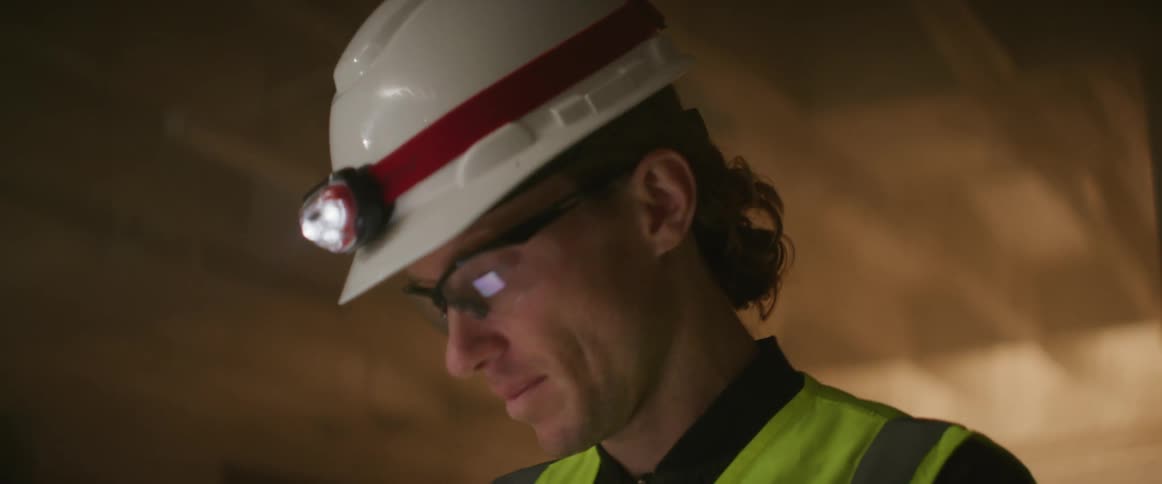 Construction worker wearing bright yellow vest and white hardhat supervising a construction site at night