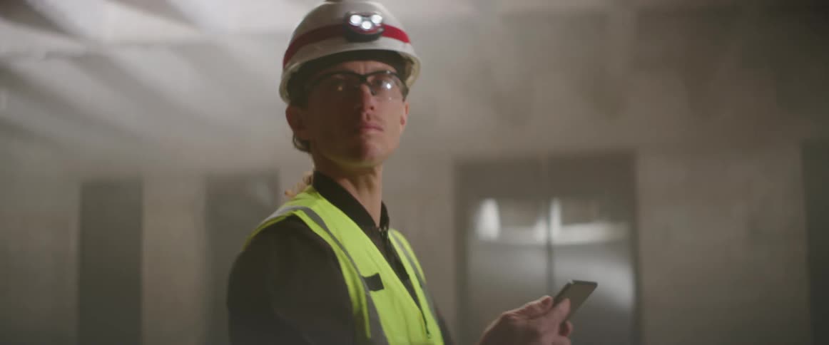 A construction worker examines a construction site while referencing his computer tablet