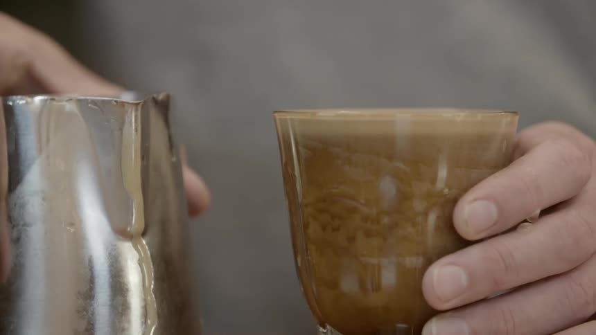 A person is holding a small pitcher and a glass