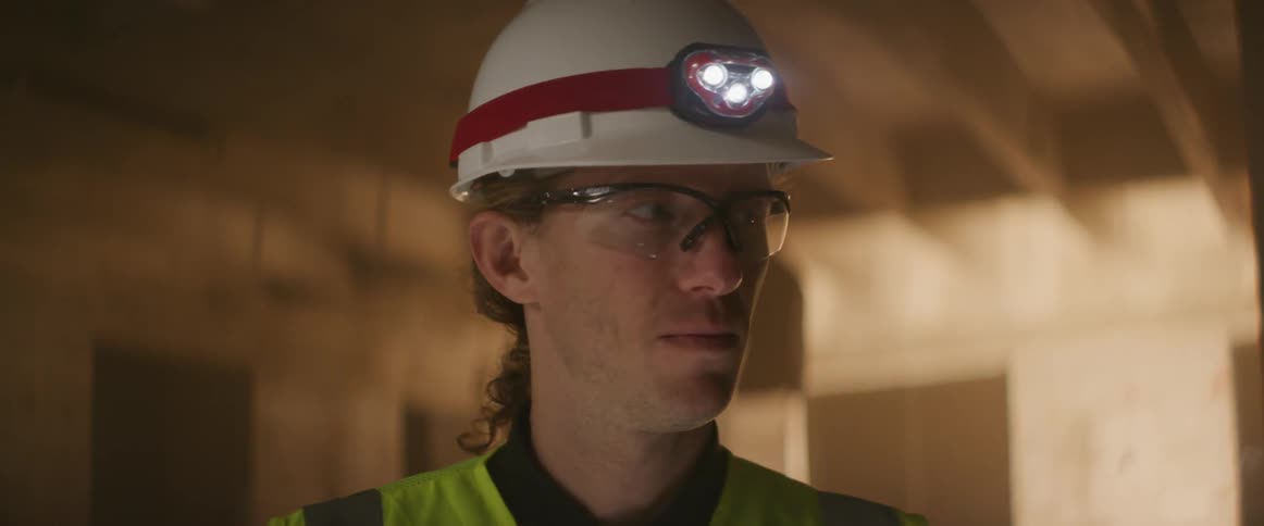 A construction worker with a helmet on stands in a building being built and looks around