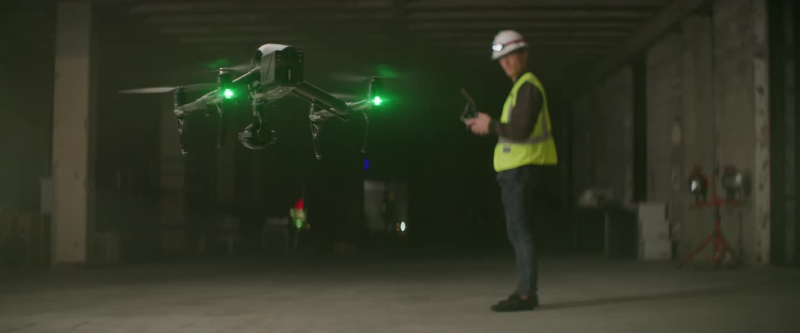 A drone with green lights rises and hovers near a man with controller