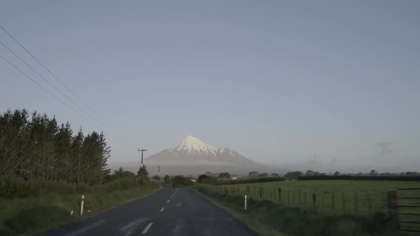 Moving down a road with grass fields and trees on either side