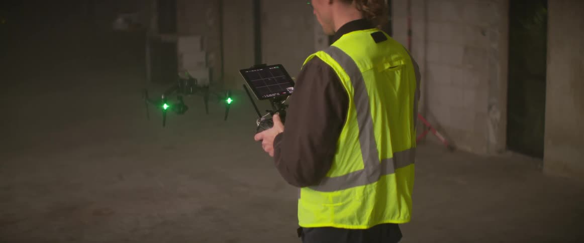 A construction worker controls a drone in an empty building