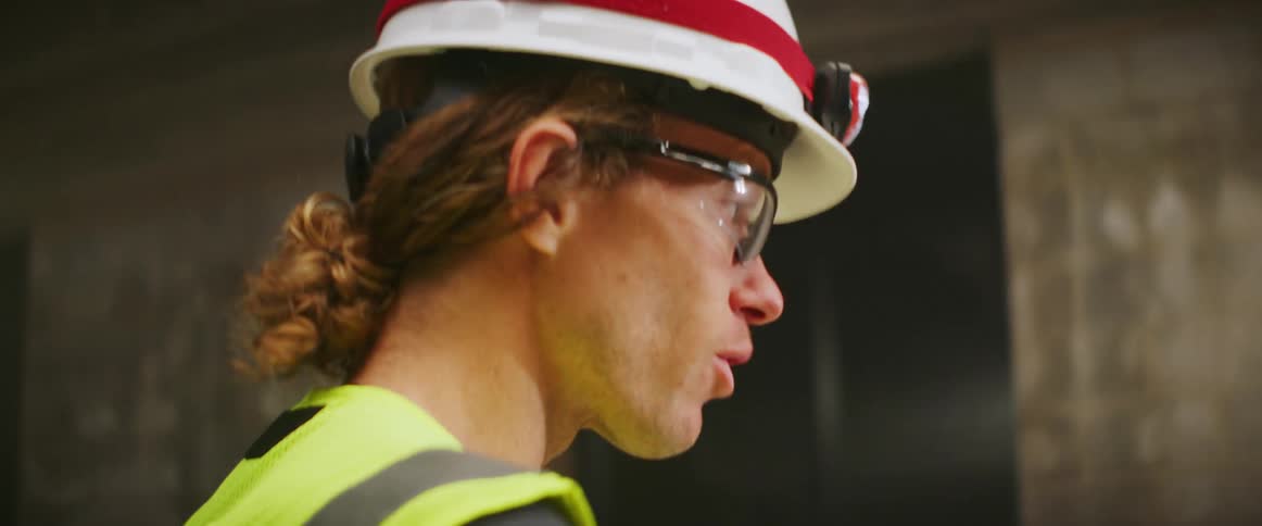 A construction worker looks at a tablet and points at cement walls as he talks to someone
