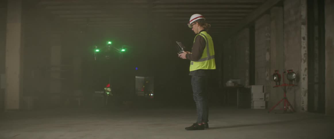 A construction worker flies a drone from the ground
