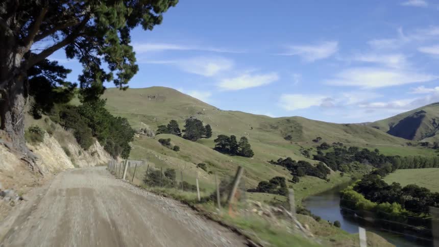 Moving along a narrow dirt road in a hilly canyon with a creek running through it