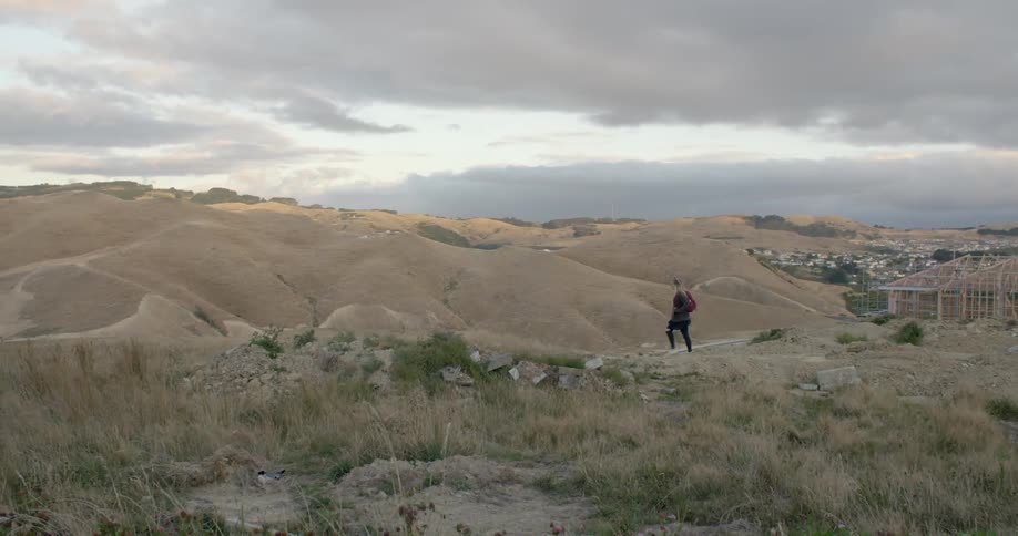 A woman walks along some hills on a cloudy day