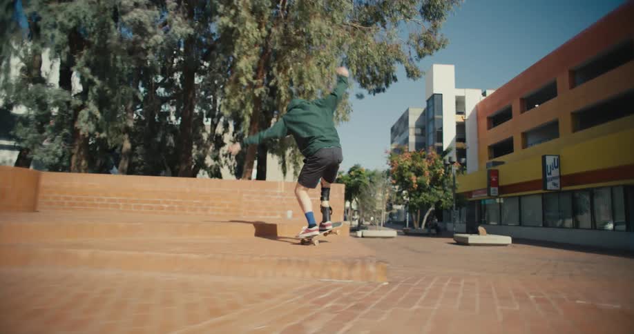 Skateboarder with prosthetic leg brace jumps off step in plaza near buildings