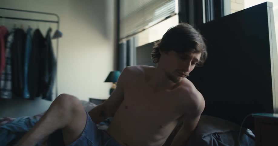 A man rises from his bed and yawns before rubbing his face