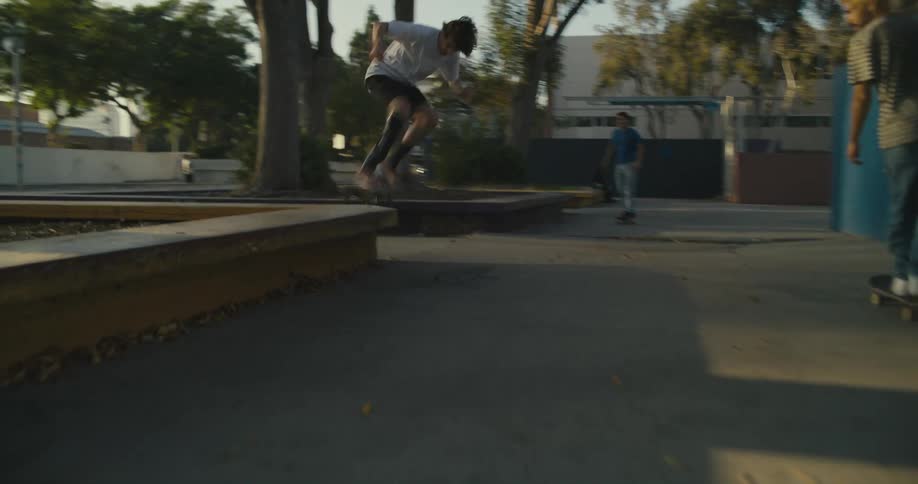 A group of people skateboard on the walkway and one performs a trick on the concrete bench