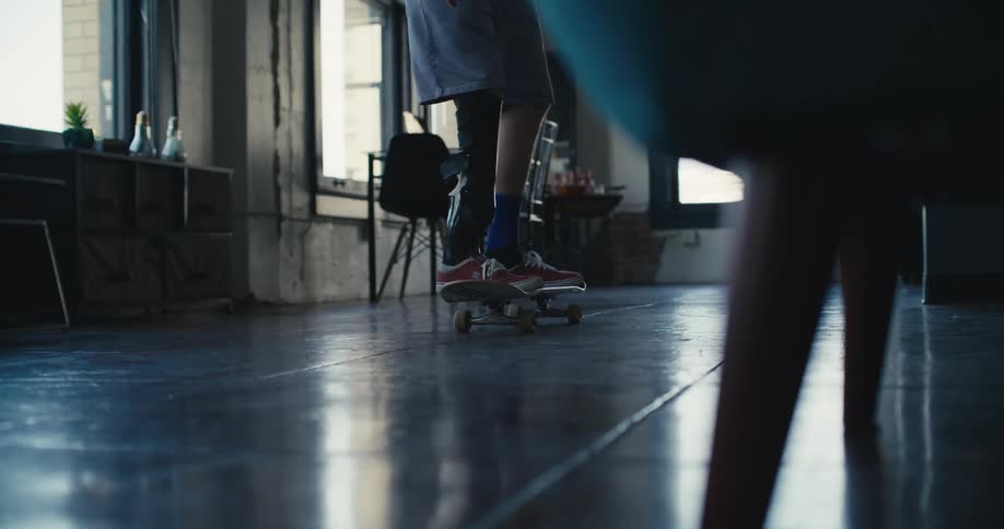 Man with prosthetic leg brace attempt to balance on skateboard in his home but falls