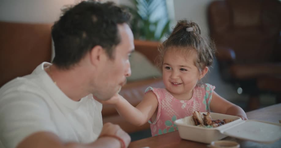 Daughter feeds father as they sit in living room smiling at each other