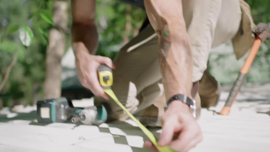 Man on a roof measuring roof tiles with measuring tape